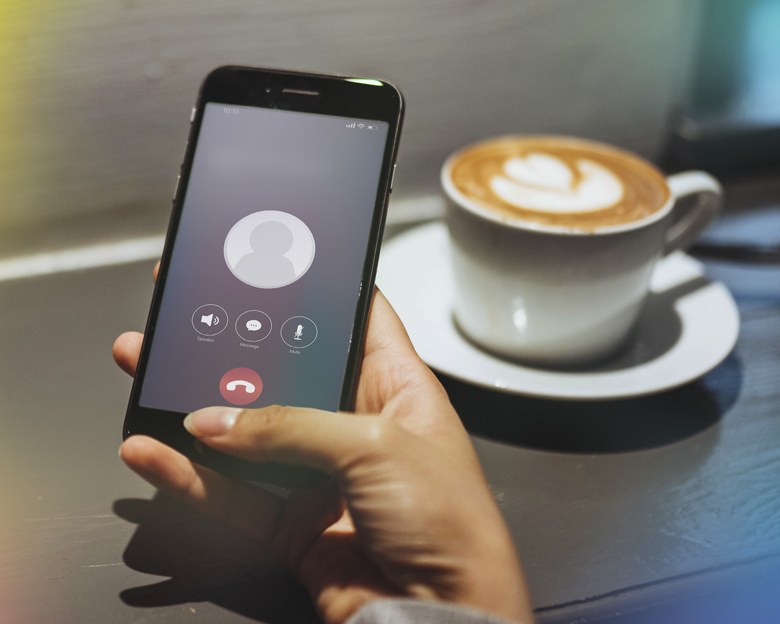 Hand holding a phone with an incoming call, beside a cup of coffee